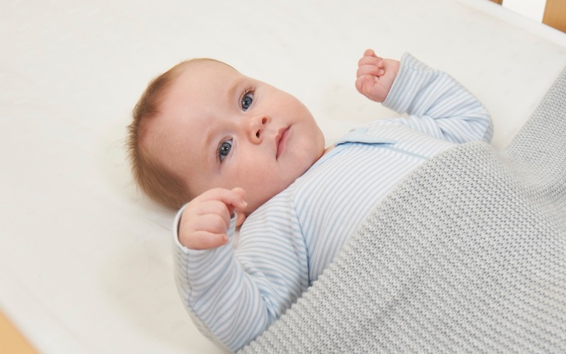 newborn sleeping on side in bassinet