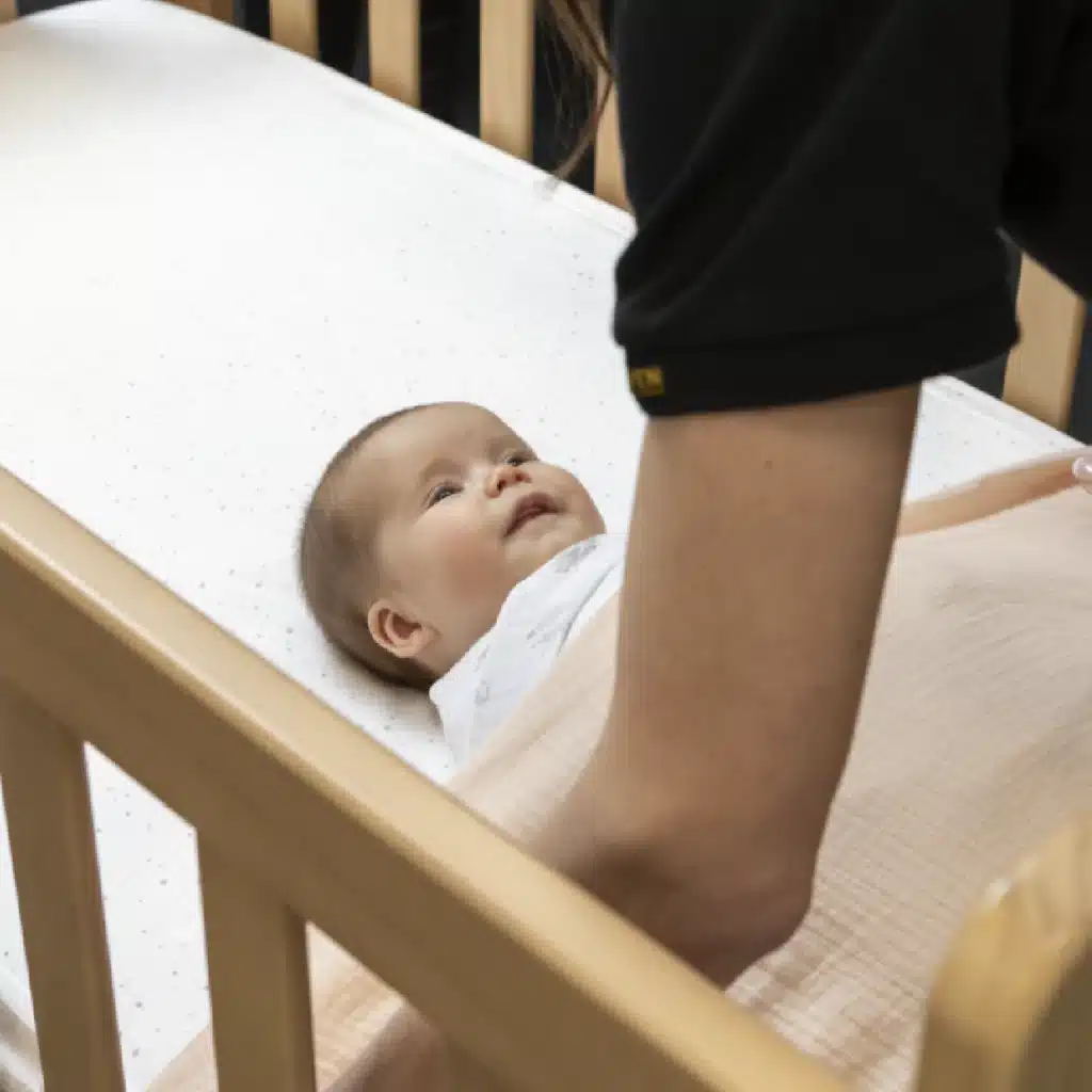 Happy baby put into a cot to sleep by a woman