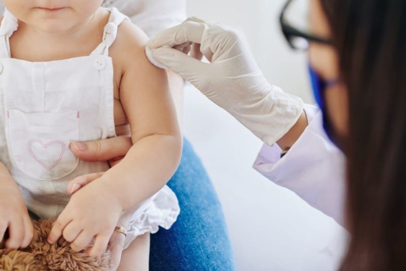 Doctor or nurse a disinfecting child's arm for vaccination