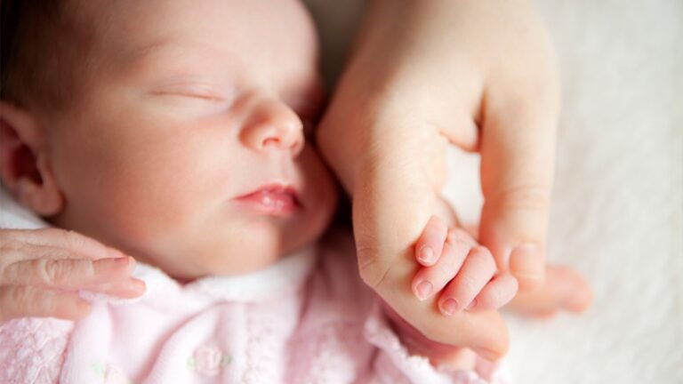 Sleeping baby holding mother's hand