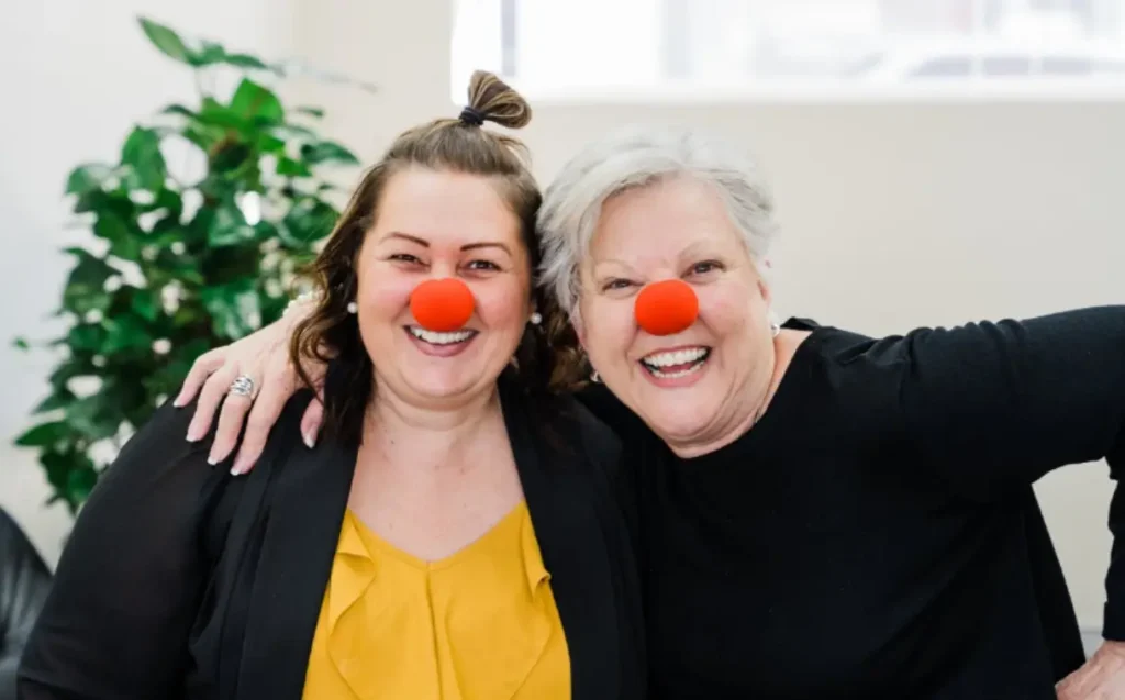 Two women smiling wearing Red Noses