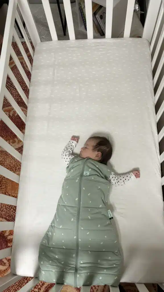 Baby sleeping in a cot wearing a sleeping bag