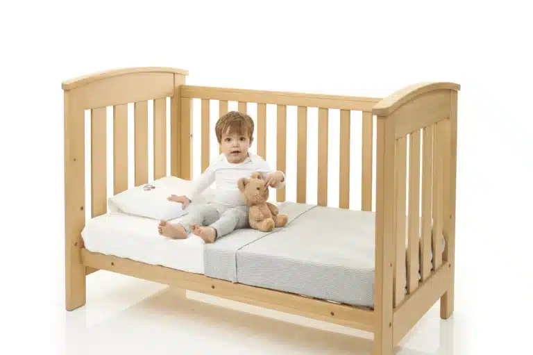 Toddler sitting up in a cot bed with a teddy bear