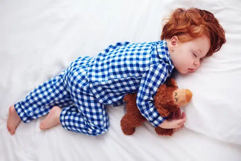 Red haired toddler sleeping in bed with soft toy
