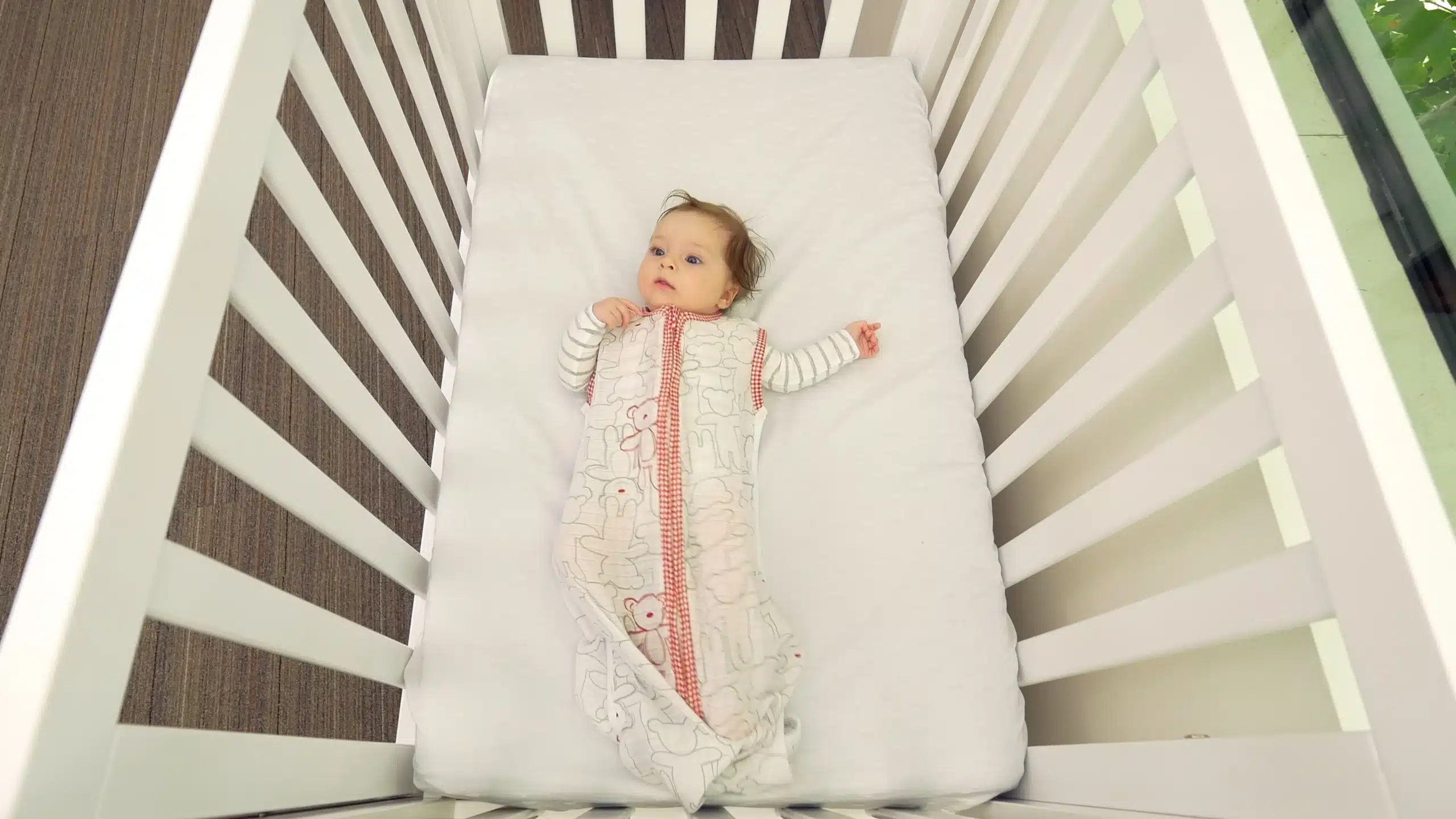 Baby wearing sleep bag lying on back in the cot