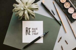 Flat lay of art materials featuring a recycle-themed note and calligraphy tools.