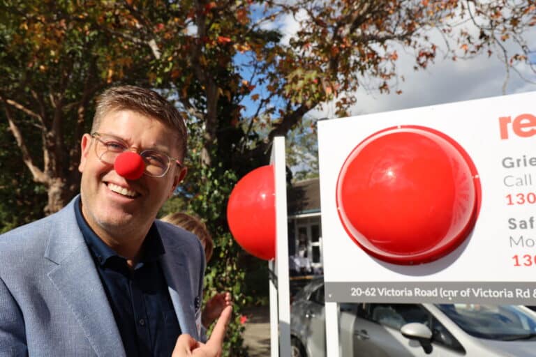 Federal Member for Federal Member for Bennelong, Jerome Laxale MP, Nick Xerakias, Board Chair of Red Nose Australia and Amy Cooper, CEO of Red Nose Australia, posing in front of Red Nose Australia's new Sydney office.