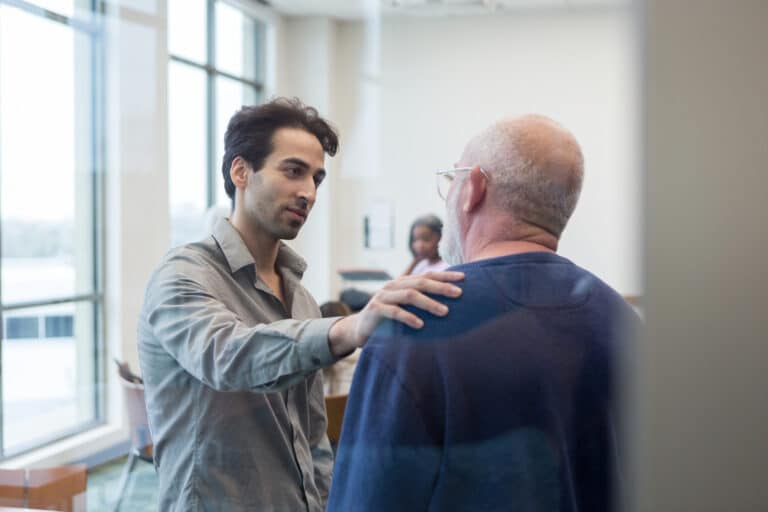 male peer supporter comforts an adult father by placing his hand on his shoulder.