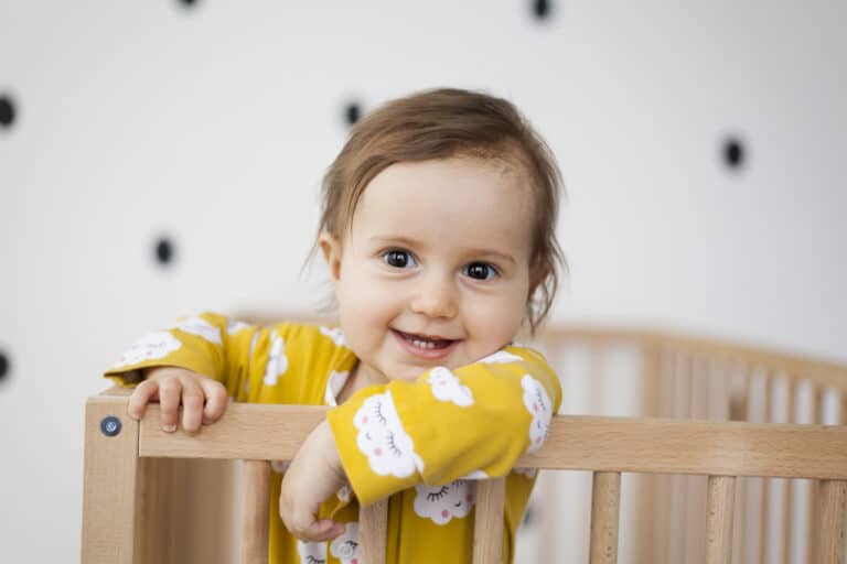 portrait of cute baby girl standing in baby crib