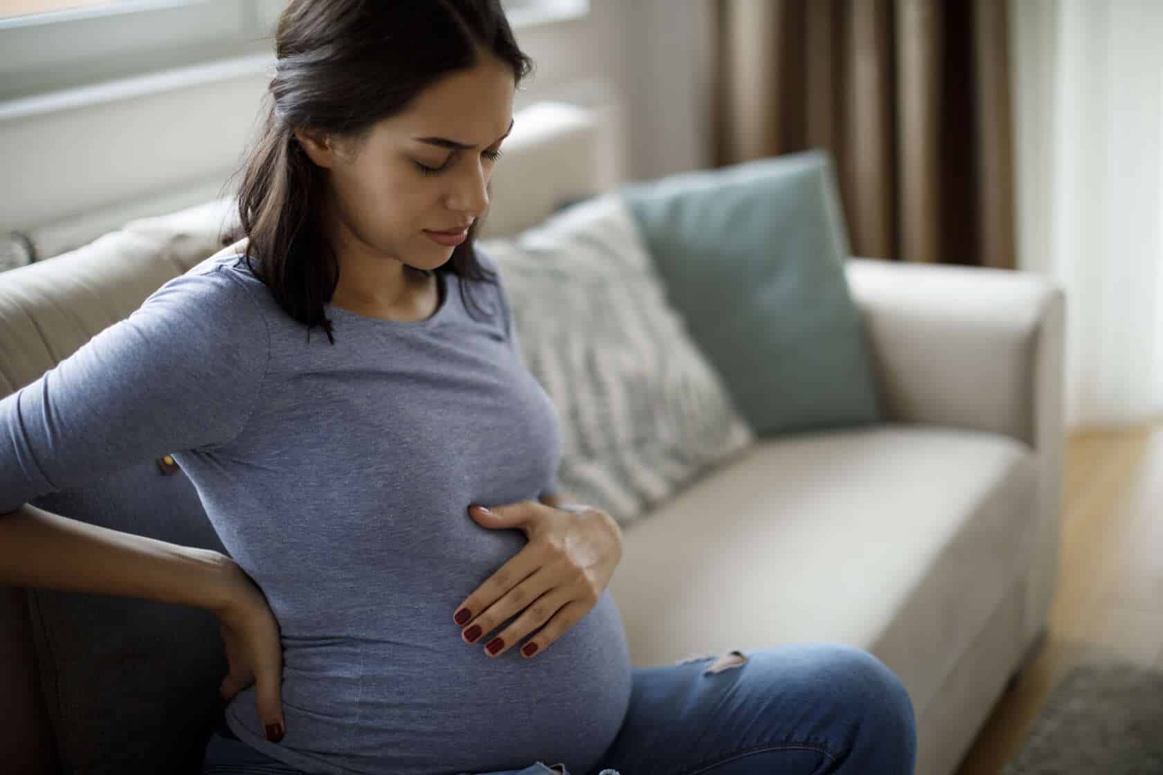 Pregnant woman on the couch with her hand on her belly, paying attention to her baby's movements