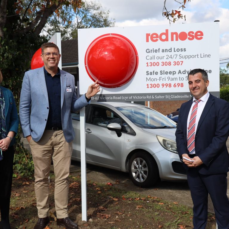 Federal Member for Federal Member for Bennelong, Jerome Laxale MP, Nick Xerakias, Board Chair of Red Nose Australia and Amy Cooper, CEO of Red Nose Australia, posing in front of Red Nose Australia's new Sydney office.