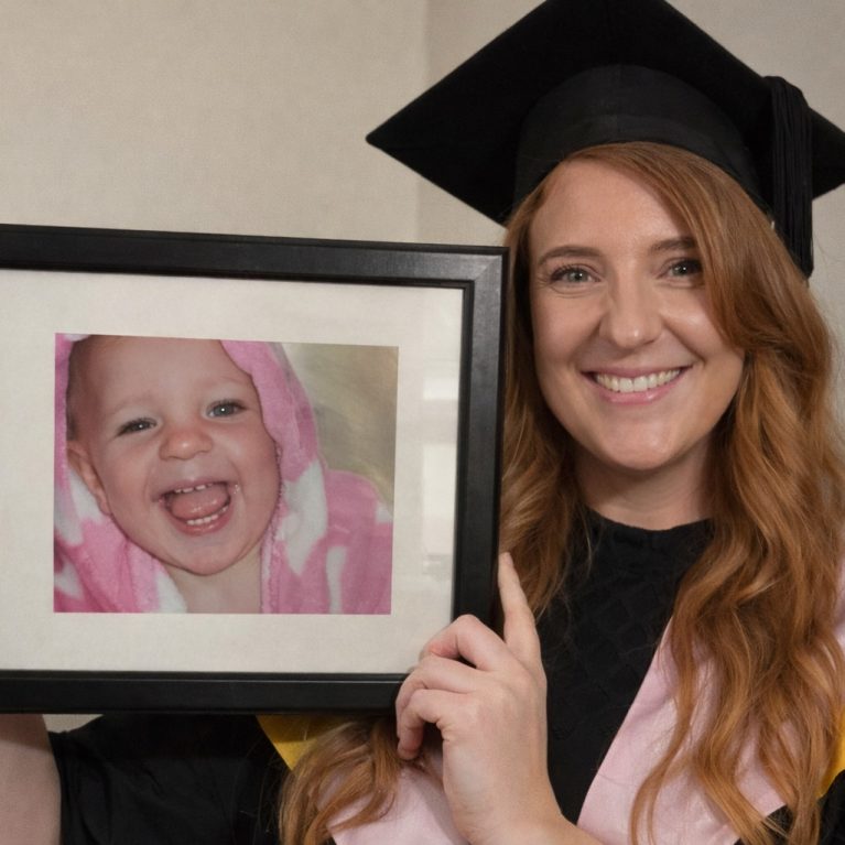 Melanie on her graduation holding photo of baby Mylee