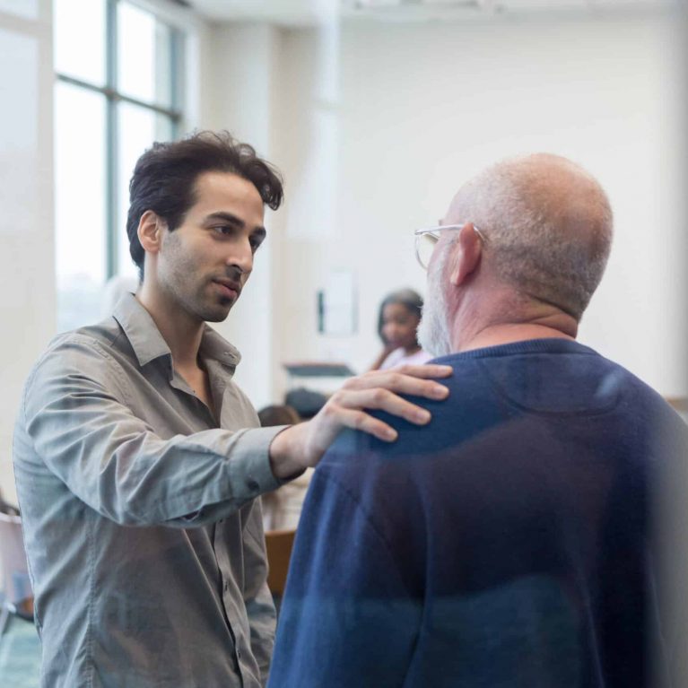 male peer supporter comforts an adult father by placing his hand on his shoulder.