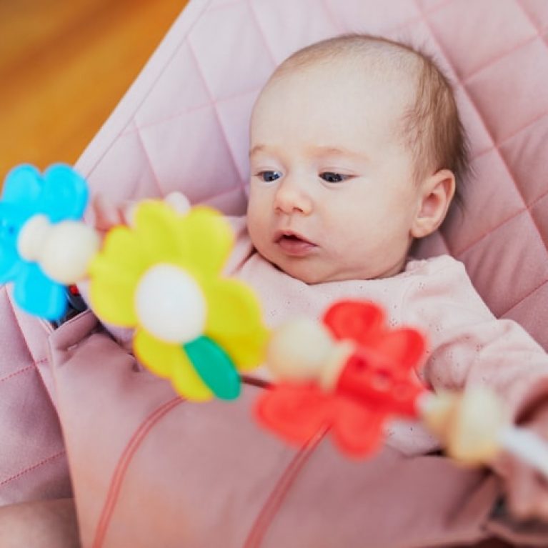 Baby girl playing with toys in bouncer